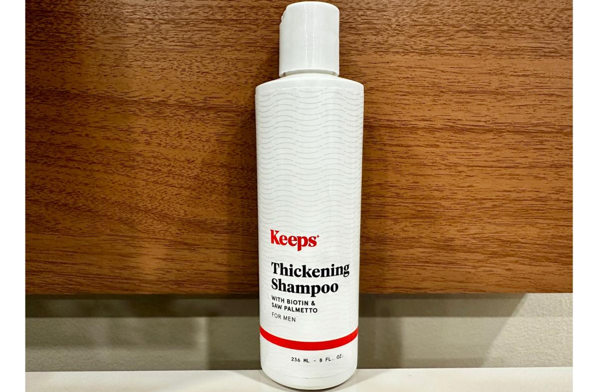A bottle of Keeps Thickening Shampoo against a wooden background.